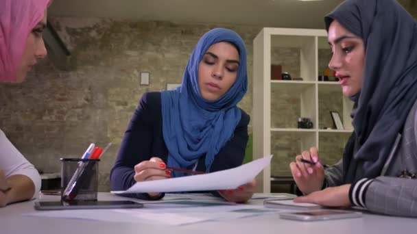 Ganska muslimska hijab kvinnor sitter på vanliga besktop och diskutera arbetande detaljer, kommunikationsprocess, mångfald — Stockvideo