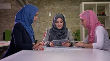 Üç Türban Arap kadın masaüstü oturma ve tablet konsantrasyon, gerçeklik, office vibes ile tutarak bazı çalışma sorunları tartışıyor