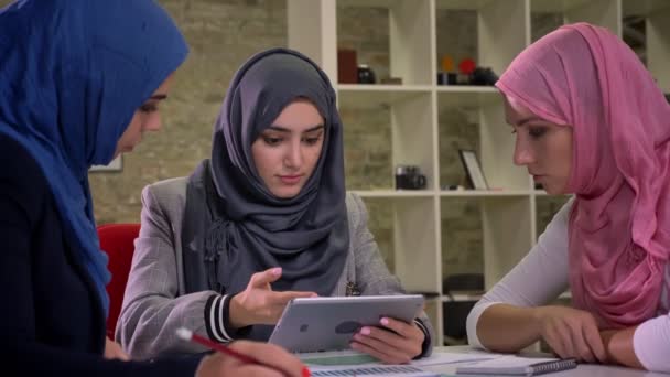 Mulheres muçulmanas hijab lindo estão sentados no local de trabalho, segurando tablet eles têm uma conversa de trabalho com rostos sérios, dentro do escritório — Vídeo de Stock