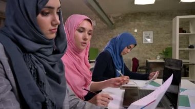 Thre güzel Türban Arap kadın doğrultusunda ortak Masaüstü, oturmak ve tuğla tuğla modern ofis içinde laptop yakınındaki çalışma
