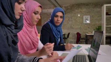 Üç eğlenceli Türban Arap kadın satırın ortak masaüstü ve laptop tuğla ofis içinde etkin tartışma ile işaret yakınında oturuyor