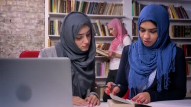 Güzel kadınların farklı hijab library laptop ve Müslüman kadın, arka plan, kapalı konsantre konuşurken yanında oturuyor