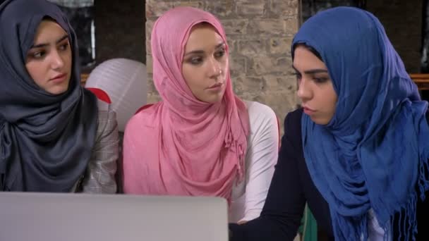 Tre belle donne hijab sono sedute a un tavolo e guardando e schermo del computer, parlando di lavoro, illustrazione per ufficio al coperto — Video Stock