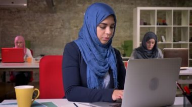 Mavi hijab Sevimli arap kadın arkasında meslektaşları ile masaüstünde oturuyor ve kamera neşeli bakıyor, tuğla noders ofis illüstrasyon.