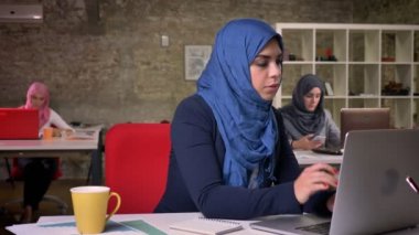 Hijabs Arap kadınlar ofiste oturuyor ve tuğla modern ofiste otururken dizüstü bilgisayar üzerinde çalışıyor