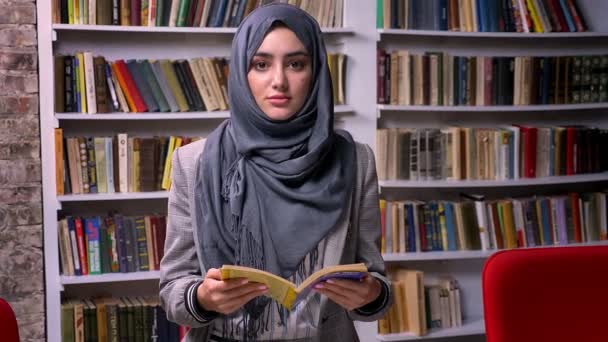 Gyönyörű Arab nő szürke hidzsáb egyhelyben és gazdaság könyv, súlyos magabiztos galce a kamerát, könyvtár, modern illusztráció — Stock videók