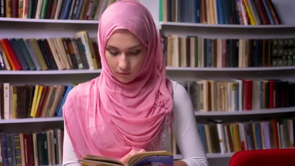 Mujer árabe feliz en hiyab rosa está de pie en la biblioteca y sonriendo alegre, humor del Medio Oriente, lugar tranquilo — Vídeo de stock