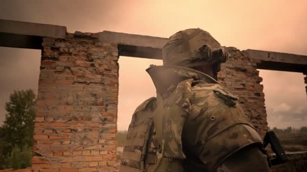 Walking soldier in camouflage is looking ahead and holding weapon, abandoned brick building illustration, rainy weather, empty space, shooting from behind — Stock Video