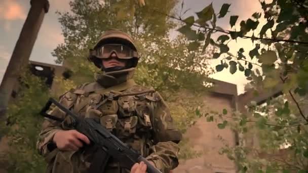 Authentischer kaukasischer Soldat in Tarnung, der durch leere Ziegelbauten und hohes Gras geht und seine Waffe kraftvoll nach vorne richtet — Stockvideo