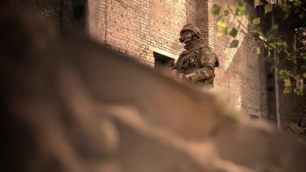 Schieten van de naar beneden hoek, Kaukasische soldaat is stil en blik op de camera, bedrijf gun, camouflage en helm dragen, bakstenen muur op achtergrond, leeg gebouw illustratie — Stockvideo