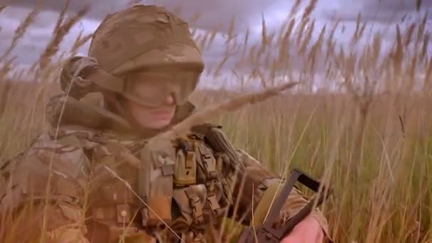 Persistent authentiek Kaukasische soldaat in de helm en camouflage dragen zitten in hoge degrasse geïsoleerd en rustig kijken naar camera, natuur achtergrond — Stockvideo