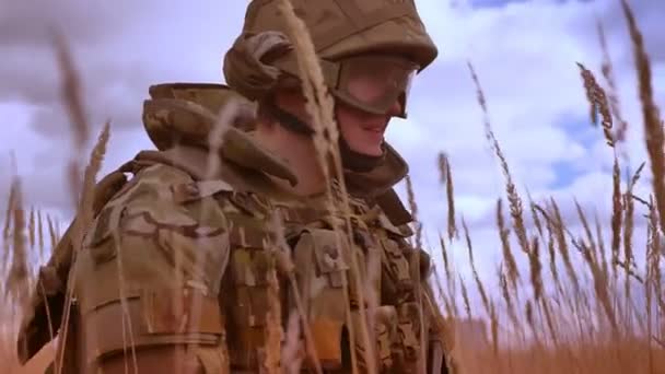 Militar hombre caucásico en camuflaje está de pie sobre una rodilla, sosteniendo pistola automática, rodeado de hierba alta, tonos escobas, viento nublado, campo vacío — Vídeo de stock