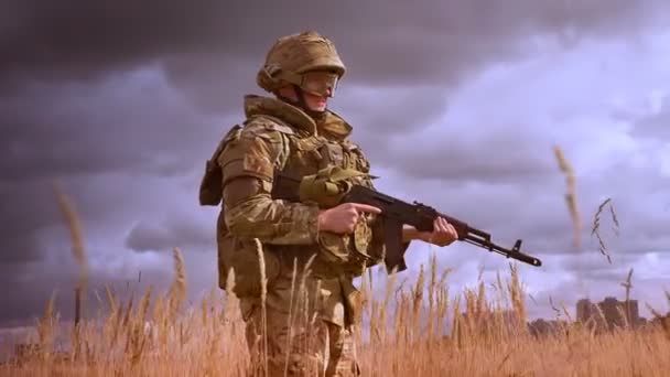 Authentische Erschießung von kaukasischen Soldaten in Tarnuniform und Helm steht und sieht Naturgebiet im hohen braunen Gras, hält Waffe in Verteidigungsposition, isoliert, verfinsterter Himmel — Stockvideo