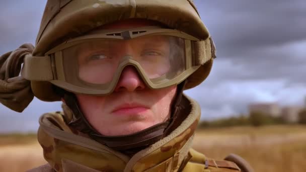 Ernstige assertief gezicht in de helm van Kaukasische soldaat stil en rondkijken, afgezonderd op tarwe achtergrond van een veld, donkere luchten achter — Stockvideo