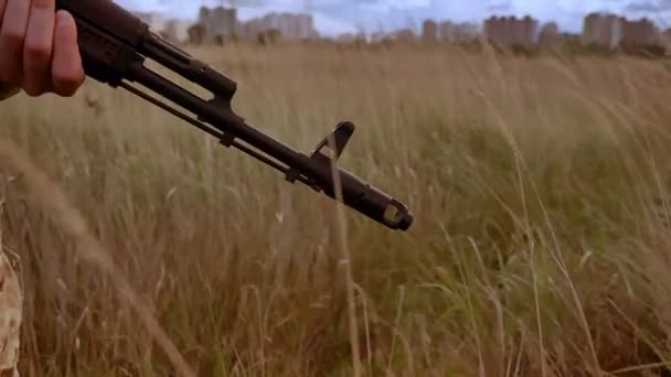 Närbild fokus automatisk pistol i händerna på stark kamouflerade soldat, stående ensam i vetefält medan vinden blåser och gräs i rörliga — Stockvideo