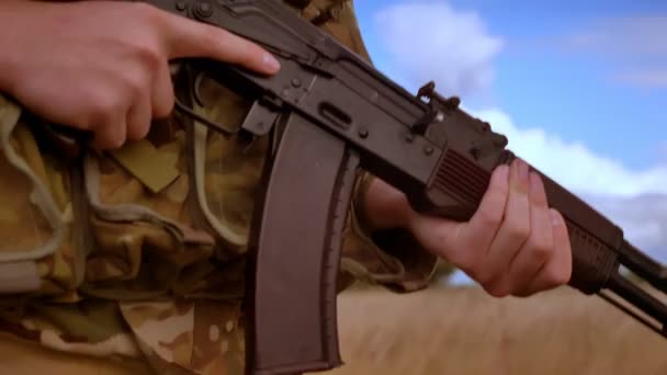 Close-up shooting of military automatic gun in hands of camouflaged soldier, walking in high grass isolated, blue skies background — Stock Video