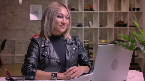 Šťastný, Kavkazský blond dívka sedí u počítače a ukazuje jako znamení na kameru v blízkosti svého počítače, uvolněný a energický — Stock video