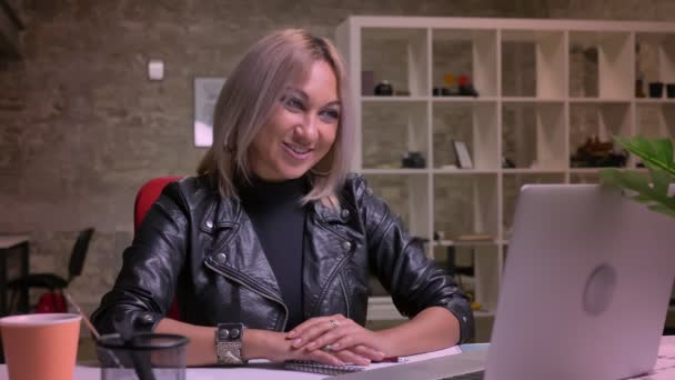 Incroyable femme blonde caucasienne heureuse a des conversations énergiques sur son ordinateur portable, illustration d'appel vidéo, tout en étant assis dans un bureau en brique moderne isolé — Video