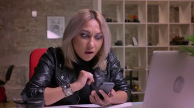 Keyifli beyaz sarışın kadın onun smartphone ışık modern tuğla bina, office arka plan, tüyler ürpertici izole otururken swiping