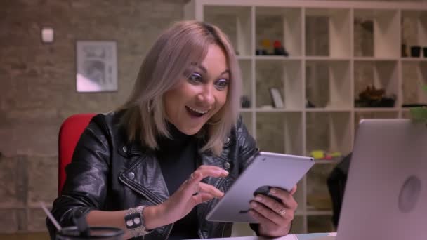 Uśmiechający się zaskoczony wygląd Blondynka kaukaski kobieta interesu, który jest za pomocą tabletu, energicznie i szczęśliwie będąc indoot w Cegła odizolowane, nowoczesne office odprężający ilustracja — Wideo stockowe