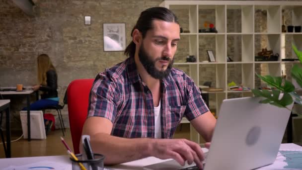 素敵なひげとハンサムな caucasain 作業の男性が彼のデスクトップに座っている、コンピューターで彼の仕事を停止し、魅力的なカメラ見て笑顔、屋内図オフィス スタイル — ストック動画