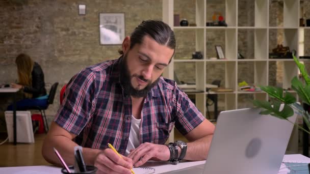 Concentré sur son écriture caucasien gars est assis cna regarder précisément ses notes tout en étant assis sur le bureau, illustration de travail, style décontracté — Video