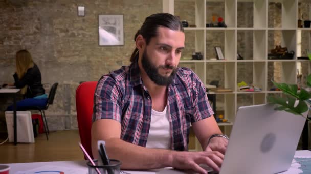 Homem caucasiano decepcionado está fazendo pausa de usar laptop e desesperadamente olhando para a tela enquanto sentado no frio escritório de tijolo leve — Vídeo de Stock