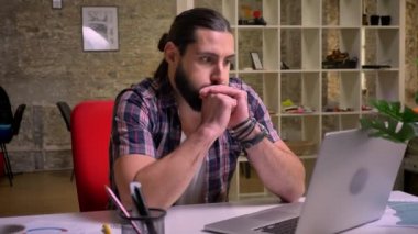 Siyah sakallı yakışıklı beyaz işadamı durulması ekrana bakarak ve tuğla ofiste otururken çalışma zamanı sırasında düşünme arka plan ışık