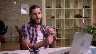 Casual komik beyaz adam uzun saçlı ve siyah sakallı laptop, rahat ve mutlu ruh hali, kapalı, açık arka plan Masaüstü, otururken dans ediyor