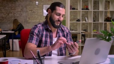 Harika yaratıcı cauasin erkek siyah sakallı nad uzun saçlı telefonunu swiping oturma kapalı, ofis arka plan, işçiler