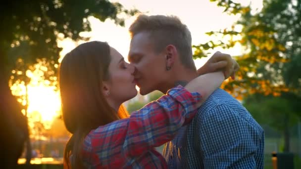 Casal encantador está se beijando calmamente enquanto está em pé no belo pakk ao ar livre, luzes solares, olhar casual — Vídeo de Stock
