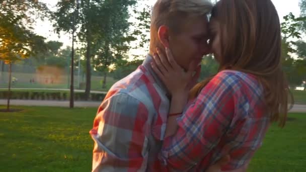 Красивая пара поцелуев смотрят друг на друга и стоят весело и спокойно в удивительном парке, окруженные деревьями и зеленой травой, находясь вместе друг с другом — стоковое видео