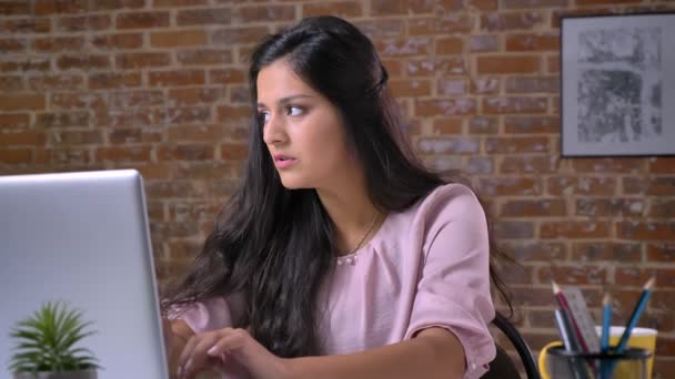 Inteligente bela cauasn senhora está digitando em seu laptop concentrado enquanto sentado no escritório de tijolos em seu desktop, sendo produtivo e energético — Vídeo de Stock