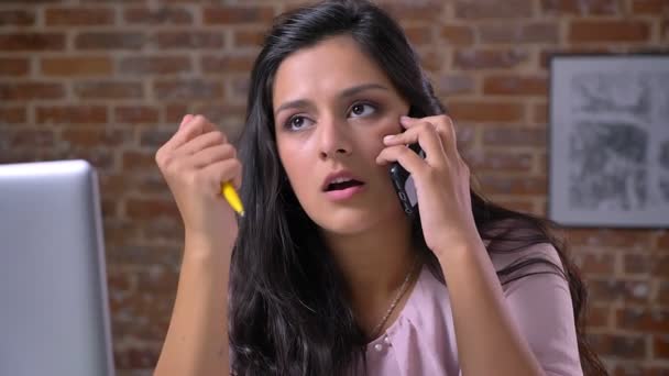 Gros plan beau visage de travail et parler caucasienne jolie femme, traînant dans la vidéo de bureau, près de son ordinateur portable sur fond de brique — Video