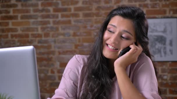 Χαλαρωτικό συνομιλία μέσω τηλεφώνου του Καυκάσου ωραία γυναίκα που απολαμβάνει την ώρα που καθόμουν στην επιφάνεια εργασίας, χαμογελώντας ευτυχώς, όντας σε μοντέρνο κόκκινο γραφείο — Αρχείο Βίντεο