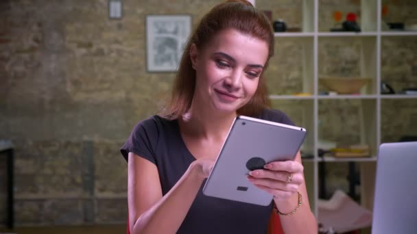 Awesome kaukasische Ingwerweibchen zeigt Blue Screen auf dem Tablet vor der Kamera und sieht glücklich und kühl aus, während sie drinnen im modernen Büro sitzt — Stockvideo