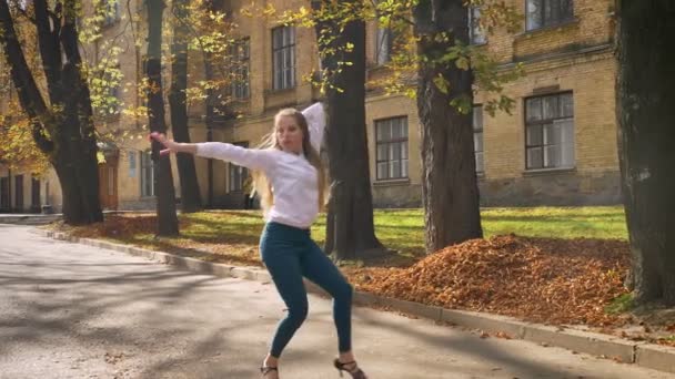 Impressionante femmina caucasica con lunghi capelli biondi sta ballando latina per strada, background universitario — Video Stock