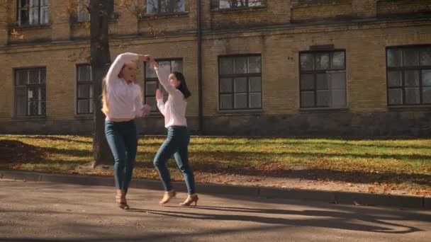 Две удивительные кавказские девушки танцуют вместе на улице в солнечный день, будучи вдохновленными и счастливыми, демонстрируя различные движения на фоне зданий — стоковое видео