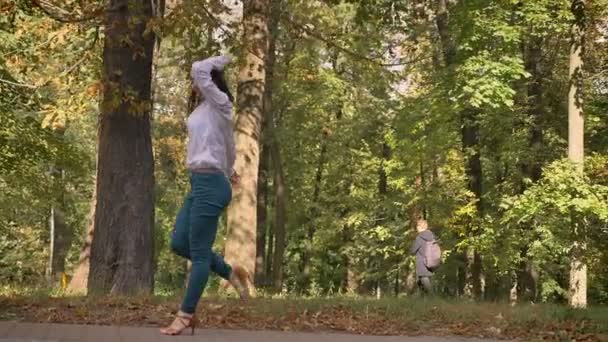 Happy Dance de belle fille brune caucasienne qui se déplace artistiquement vers l'arrière dans un parc ensoleillé sur fond d'arbres, image brillante, illustration lumineuse — Video