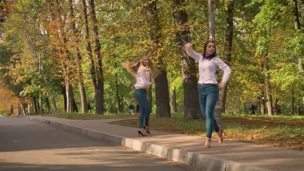 可爱的白种人金发女郎和褐发女郎正在同步跳舞的人行道上, 绿色公园后面, 阳光插图, 公共场所 — 图库视频影像