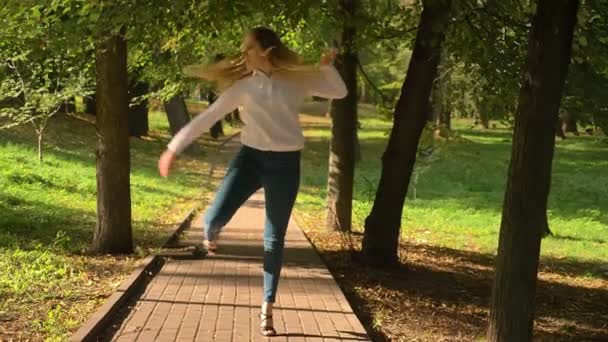 Красивая блондинка-кавказка практикует латинский танец и делает шаги от камеры к красивому летнему зеленому парку, двигаясь по следу — стоковое видео