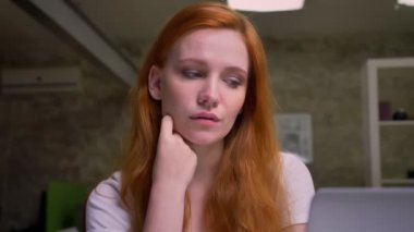 Kızıl saçlı caucasin kadının güzel yüzü ve düşünceli duyguları ile çekim, sakin bir şekilde aşağı ve kamera modern ofiste otururken bakarak yakın çekim.