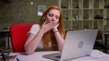 Esneme beyaz Kızıl saçlı kadın Masaüstü, yaratıcı Studio tuğla ofiste otururken dizüstü bilgisayar ekranına bakarak