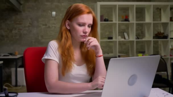 Tosse trabalhando menina gengibre com aparência caucasiana está digitando no teclado e olhando para a tela, estar envolvido no processo de trabalho, ilustração indoor — Vídeo de Stock