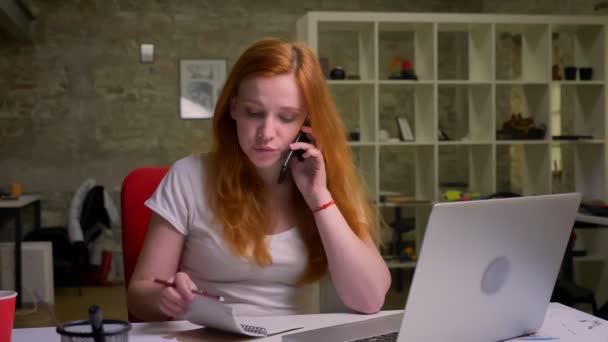 Fleißige Ingwer kaukasische Geschäftsfrau telefoniert und checkt Nitten in der Nähe von Laptop, Büro Illustration, hübsche Person — Stockvideo