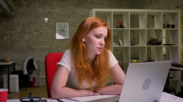 Emin beyaz zencefil kadın video seslenmek üstünde laptop geçiriyor ve oturma rahat doğrusu, seyir İşyerinde ışık ofis kapalı — Stok video
