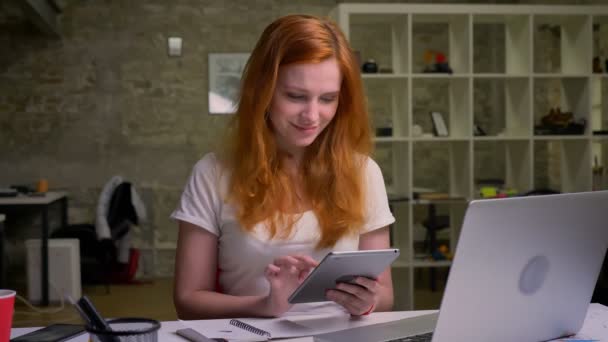 Концентрированная рыжая кавказка Диплу тащит планшет, сидя за столом в офисе модера, бумагах и рабочем эквиваленте — стоковое видео