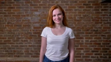 Muhteşem rahat kafkas kadın mükemmel Kızıl saçlı ve dostça utangaç gülümseme, ayakta seyir tuğla duvar sna üzerinden kameraya, mutlu vibes rahat.
