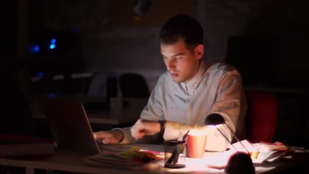 Knappe Kaukasische moderne man is laptop toetsenbord en uitzetten van de computer, afwerking van zijn werk, 's avonds laat en duisternis in kantoor — Stockvideo