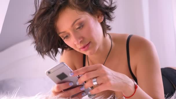 Caucasienne fille sexy en lingerie noire est couché sur une couverture moelleuse à l'aide d'un smartphone, dactylographier du texte, tentation, flirt — Video